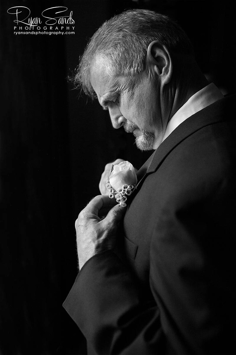 Grand Summit Hotel Wedding - A groom's father pins his flower to his jacket under the light of an open window.